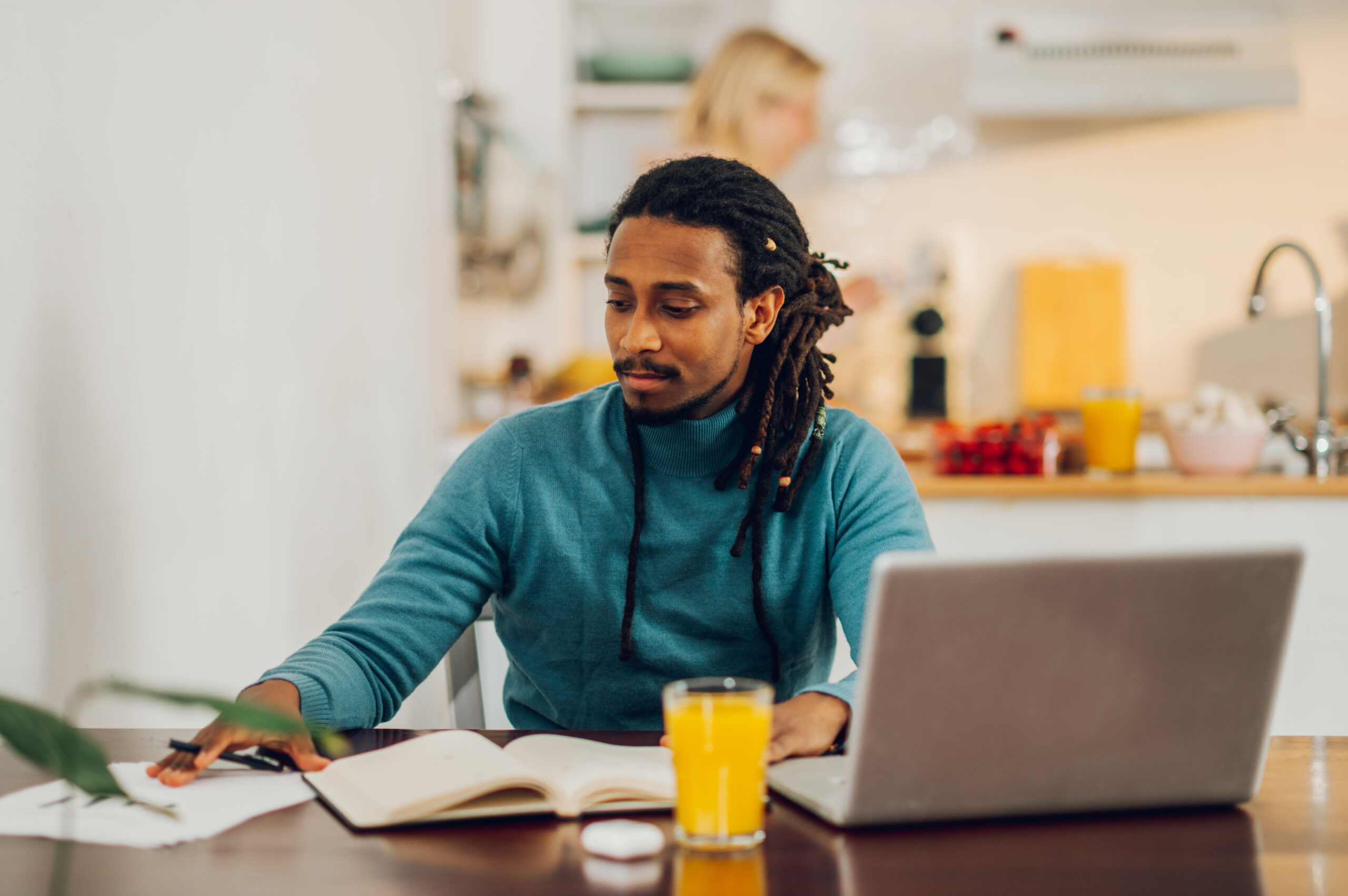 An Arabic data scientist is sitting at home and working on paperwork and data entry. A multicultural remote worker is working with paperwork and documents while using a laptop from home.