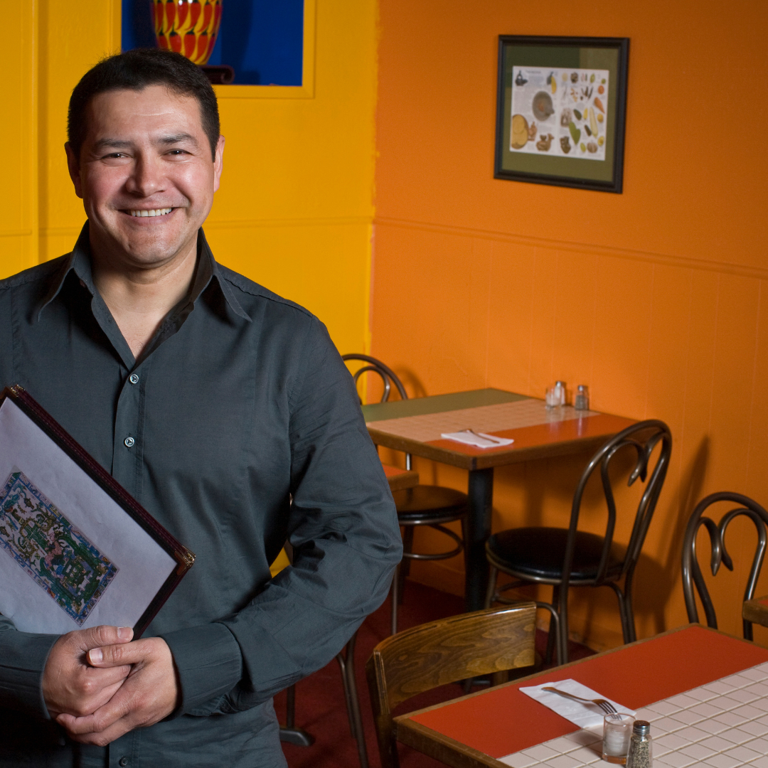 restaurant owner standing inside of his restaurant holding framed art